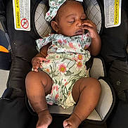 Cyanna is registered to the contest to win money with this photo: baby, infant, sleeping, car_seat, floral_outfit, headband, black_skin, peaceful, cute, child, footwear_none, indoors, seat_belt, warning_label, small_person, portrait, clothing, hands, toes, resting