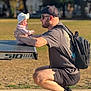 Michelle joined the competition — help win amazing prizes! baby, backpack, beard, casual_clothing, child, daylight, glasses, hat, holding, man, outdoor, park, ping_pong_table, shoes, shorts, smile, squatting, sunlight, table, tshirt