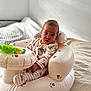 baby, bed, blanket, child, cozy, cute, floral_pattern, home, indoor, infant, inflatable_chair, looking_at_camera, nursery, pajamas, person, seated, soft_lighting, striped_clothing, toy, young_child