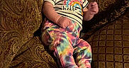 Delilah is registered to the contest to win money with this photo: baby, infant, child, portrait, smiling, sitting, couch, cushions, purple_bow, headband, rainbow_clothing, striped_shirt, colorful_pants, socks, indoors, living_room, textured_fabric, furniture, cozy, happy
