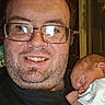 adult, baby, newborn, father, parent, portrait, selfie, smiling, sleeping, glasses, beard, indoor, close_up, holding, infant, white_clothing, family, face, window, photograph