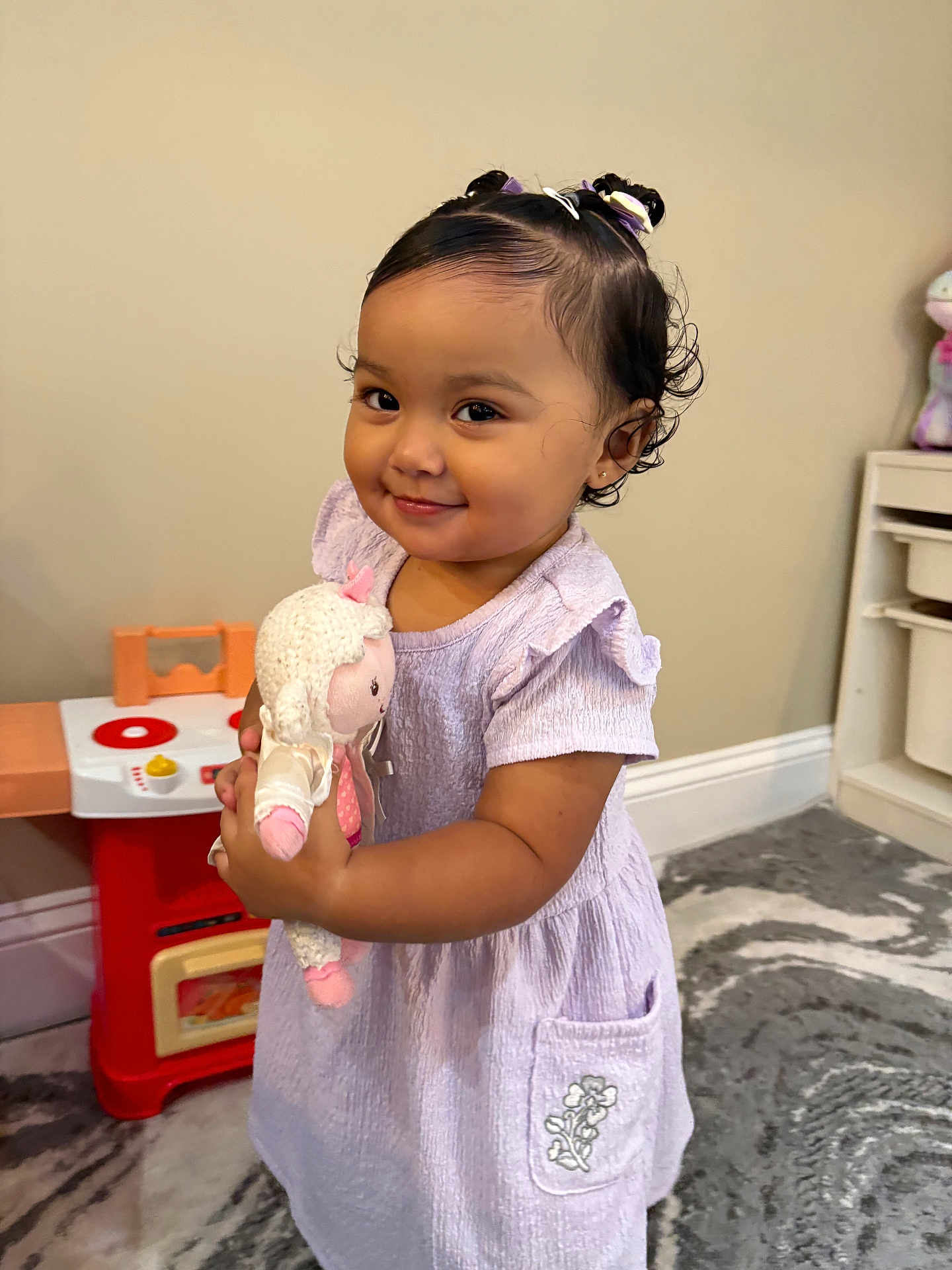 Kehlani Rose is registered to the contest to win money with this photo: toddler, child, smile, dress, toy, doll, indoor, playroom, hair_buns, curly_hair, carpet, furniture, cute, happy, person, young_child, plush_toy, purple_dress, home, floor