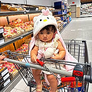 Kehlani Rose joined the competition — help win amazing prizes! toddler, child, shopping_cart, grocery_store, bread, stuffed_toy, hooded_blanket, clothing, footwear, sandals, person, aisle, shelf, food, shopping, supermarket, cute, serious, indoor, baby