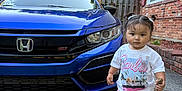 Kehlani Rose joined the competition — help win amazing prizes! toddler, child, car, blue_car, honda, si_badge, sidewalk, house, brick_wall, trees, outdoor, daylight, concrete, stick, white_shoes, pink_shorts, white_tshirt, pigtails, curly_hair, portrait