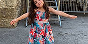 Ohana participe au concours pour gagner de l'argent avec cette photo : child, girl, dress, colorful, long_hair, smiling, outdoor, stone_wall, metal_stairs, pavement, sandals, sunny, greenery, tree, fence, building, happy, arms_outstretched, daylight, portrait