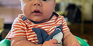 Maliki joined the competition — help win amazing prizes! baby, child, infant, seat, green, striped_shirt, indoor, curious, wide_eyes, hands, face, expression, blurred_background, furniture, cushion, sitting, person, young, close_up, casual