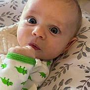 Zaiden is registered to the contest to win money with this photo: baby, infant, face, onesie, dinosaur_pattern, hand, blue_eyes, blanket, close_up, portrait, cute, child, soft_lighting, indoor, expression, newborn, skin, sleepwear, resting, curious