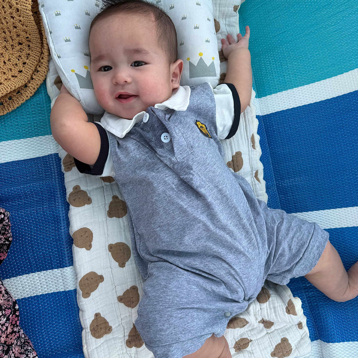 Aiden Thon is registered to the contest to win money with this photo: baby, infant, smiling, blanket, pillow, clothing, romper, face, arms, legs, foot, striped_mat, bear_pattern, blue, white, grey, cute, happy, lying_down, indoors
