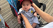 Aiden Thon is registered to the contest to win money with this photo: adult, baby, bag, blue_bag, boardwalk, cap, casual_clothing, child, daylight, expression, flip_flops, hands, outdoor, person, red_cap, seated, striped_pants, stroller, summer, wooden_floor