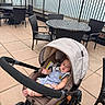 Aiden Thon is registered to the contest to win money with this photo: baby, stroller, outdoor, patio, wicker_chair, table, baby_bottle, urban, fence, concrete_floor, infant, child, person, seated, canopy, footwear, clothing, daylight, relaxing, curious