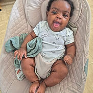 Léana a rejoint le concours — aidez-le/la à gagner de superbes lots ! baby, infant, child, smiling, onesie, curly_hair, baby_seat, quilted, beige, soft_toy, green_cloth, cute, happy, indoors, floor, wooden_floor, skin, expression, sitting, person