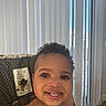 toddler, child, smiling, curly_hair, high_chair, indoor, face, happy, baby_food, teeth, patterned_fabric, window_blinds, person, cute, young_child, skin, portrait, seat, tableware, natural_light