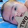 baby, infant, two_months, wooden_sign, blue_blanket, close_up, face, hand, eyes, soft_texture, colorful_ball, background_blur, cute, newborn, lying_down, portrait, skin, child, toddler, indoors