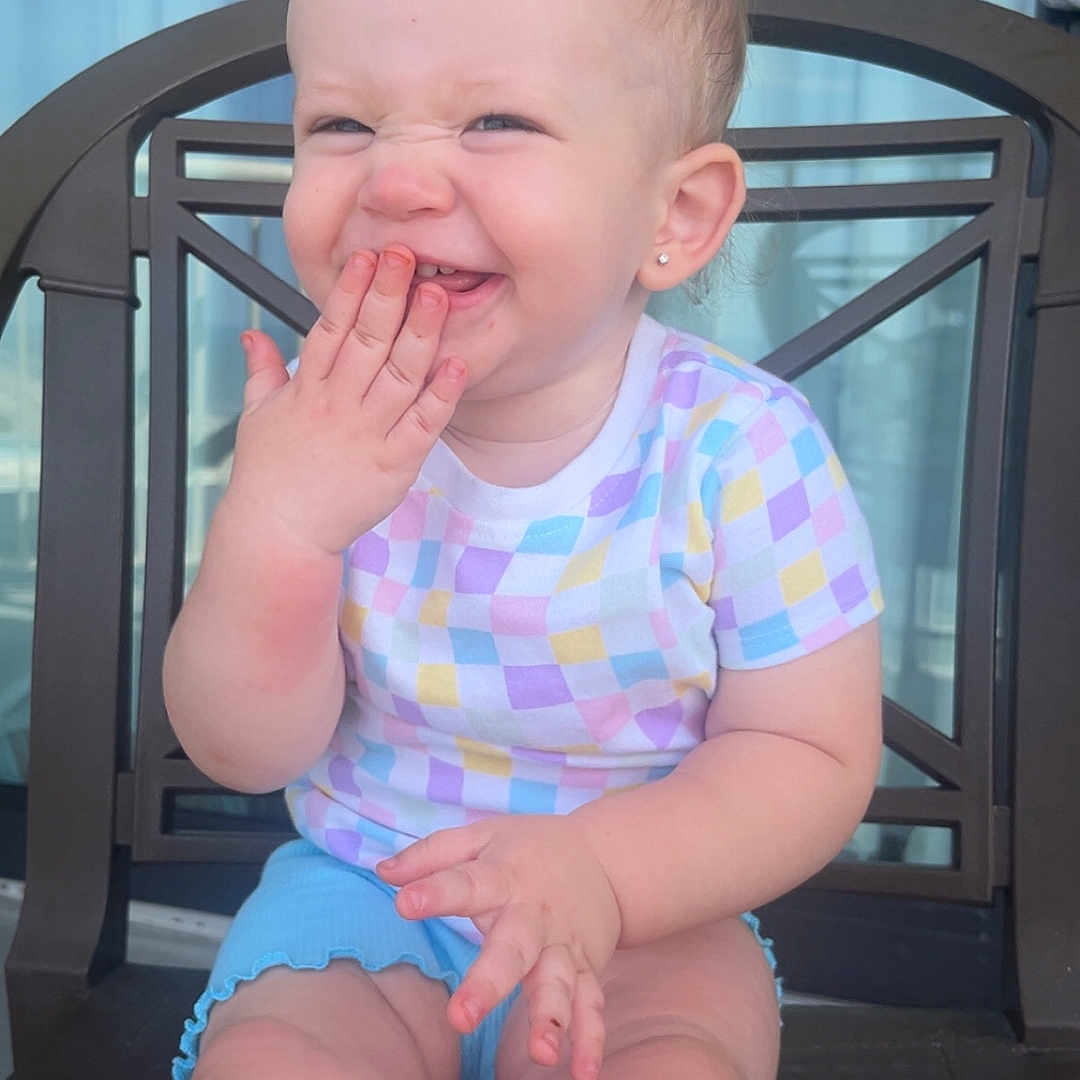 Emilee is registered to the contest to win money with this photo: baby, chair, child, clothing, cute, earring, expression, face, hand, happy, indoor, laughing, person, playful, ponytail, portrait, shorts, sitting, skin, smiling