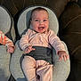 baby, infant, smiling, pink_outfit, bouncer_seat, baby_seat, couch, living_room, happy, cheerful, chubby_cheeks, bright_eyes, hands, legs, portrait, textured_fabric, stitching, seatbelt, indoor, cute