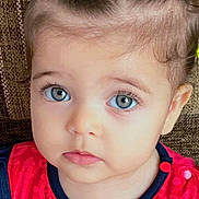 Aryem participe au concours pour gagner de l'argent avec cette photo : toddler, child, baby, face, blue_eyes, pigtails, hair_bands, red_clothing, patterned_clothing, portrait, close_up, curious_expression, sitting, indoor, brown_background, cute, young_child, looking_at_camera, soft_lighting, small_person