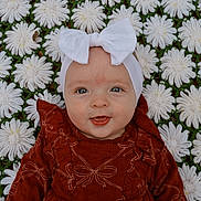 Delilah is registered to the contest to win money with this photo: baby, child, blue_eyes, headband, white_bow, smile, face, blanket, flower_pattern, texture, red_dress, ruffles, outdoor, cute, portrait, infant, lying_down, soft_lighting, closeup, happy