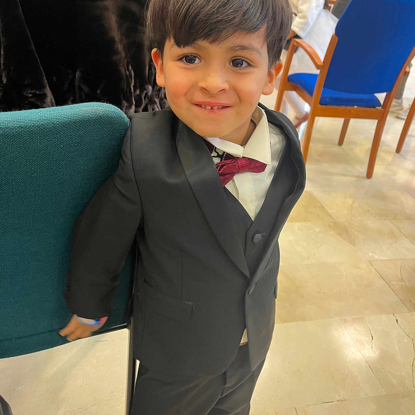 Chiheb a rejoint le concours — aidez-le/la à gagner de superbes lots ! background, bow_tie, boy, chair, child, event, face, floor, formal_clothing, hair, happy, indoors, jacket, pants, people, person, shoes, smile, suit, tile_floor