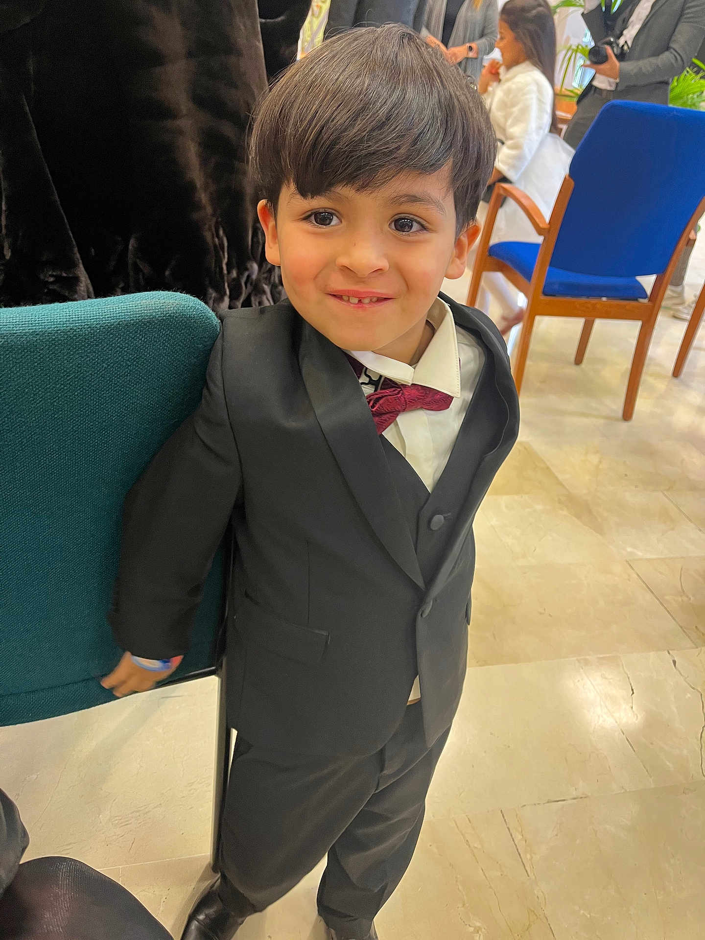 Chiheb a rejoint le concours — aidez-le/la à gagner de superbes lots ! child, boy, smile, suit, bow_tie, indoors, chair, people, floor, tile_floor, formal_clothing, hair, face, person, event, background, jacket, pants, shoes, happy