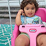 Kinsley joined the competition — help win amazing prizes! toddler, child, swing, pink_swing, curly_hair, toy, outdoor, steps, window, rope, smiling, blue_shirt, shorts, playful, face, seat, patterned_rug, person, sunset, daylight
