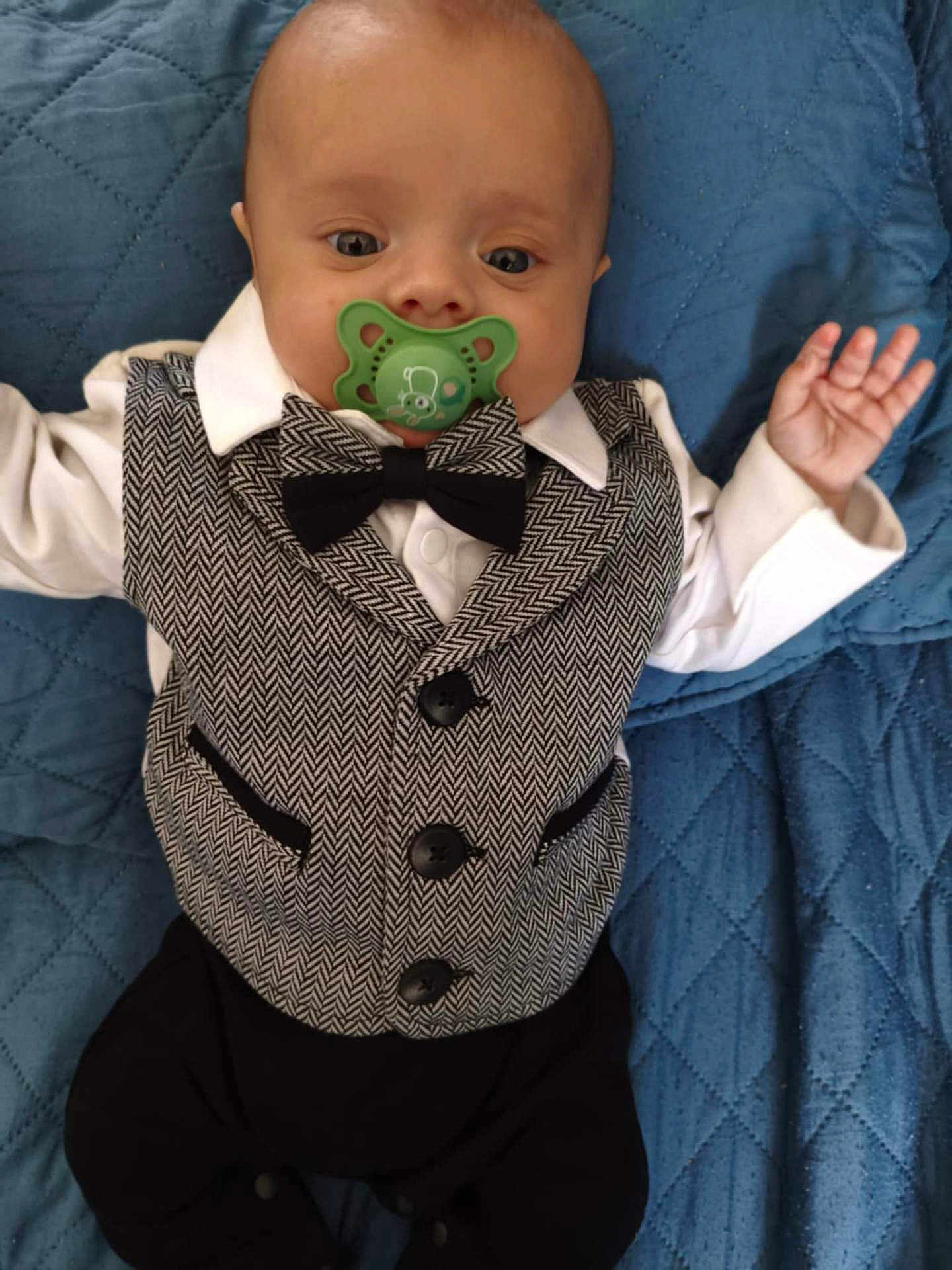 Luka participe au concours pour gagner de l'argent avec cette photo : baby, pacifier, vest, bow_tie, white_shirt, black_pants, blue_blanket, quilted_blanket, infant, lying_down, cute, face, hand, clothing, portrait, indoors, baby_fashion, child, person, newborn