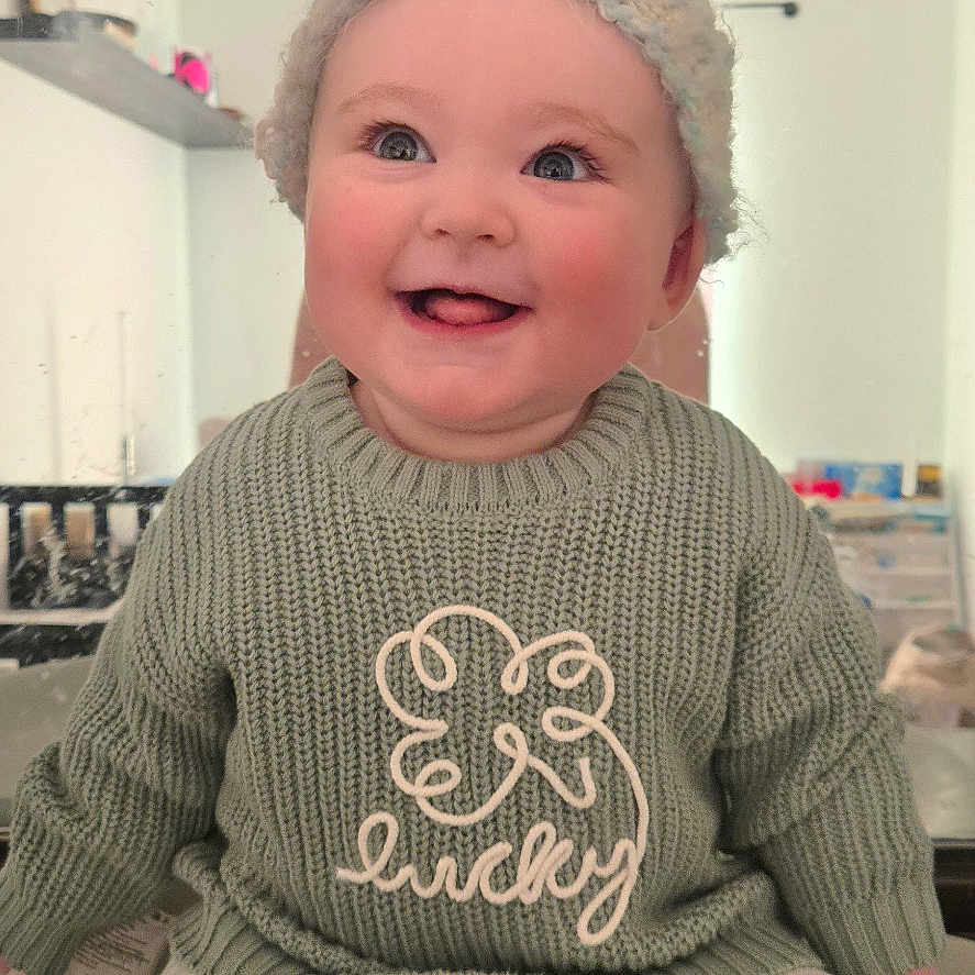 Ember Kay joined the competition — help win amazing prizes! baby, ceiling_fan, child, clothing, cozy, cute, expression, face, furniture, happy, hat, headwear, indoor, knit_sweater, person, portrait, room, sitting, smiling, striped_pants