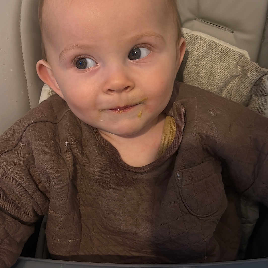 Riley is registered to the contest to win money with this photo: baby, bodypart, chair, clothing, couch, cushion, face, finger, furniture, hand, happy, head, homedecor, knitwear, person, photography, portrait, sitting, smile, sweater