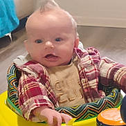Tatum is registered to the contest to win money with this photo: baby, infant, walker, toy, elephant_toy, plaid_shirt, indoor, floor, child, person, clothing, hand, face, hair, expression, seat, colorful, play, young_child, cute