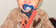 Kyrie is registered to the contest to win money with this photo: toddler, child, pacifier, smile, onesie, brown_clothing, reindeer_design, happy, cute, indoor, portrait, baby, hands, fuzzy_clothing, clip, red_strap, face, curly_hair, cozy, playful
