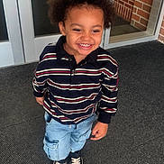 Kyrie joined the competition — help win amazing prizes! child, smiling, striped_shirt, denim_shorts, sneakers, curly_hair, happy, standing, door, glass, carpet, brick_wall, casual_clothing, young, portrait, outside, playful, cute, person, daylight