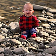 Carter is registered to the contest to win money with this photo: baby, child, infant, sitting, smiling, portrait, outdoor, river, stream, water, rocks, pebbles, riverbank, nature, red_sweater, checkered_clothing, blue_pants, red_socks, daylight, photography