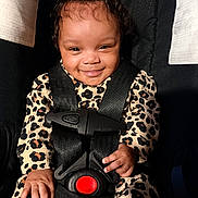 Raiyn is registered to the contest to win money with this photo: baby, child, smiling, car_seat, safety_harness, leopard_print, bow, cute, happy, infant, clothing, black, red_button, seatbelt, portrait, indoors, person, face, hand, young