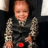 baby, child, smiling, car_seat, safety_harness, leopard_print, bow, cute, happy, infant, clothing, black, red_button, seatbelt, portrait, indoors, person, face, hand, young