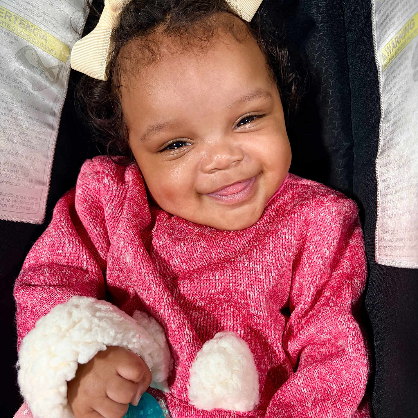 Raiyn joined the competition — help win amazing prizes! baby, smiling, child, pink_sweater, bows, curly_hair, pacifier, car_seat, cozy, cute, infant, happy, portrait, clothing, hand, face, indoor, sitting, safety_warning, yellow_bows