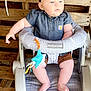 baby, baby_seat, bow, casual_clothing, child, closeup, curious, cushion, cute, denim_shirt, earrings, feet, headband, indoor, infant, pale_skin, sitting, small_toy, toy, wooden_background