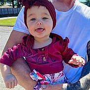 Hileigh is registered to the contest to win money with this photo: baby, child, person, adult, tattoo, outdoor, sunlight, clothing, headwrap, smiling, tongue_out, holding, arm, white_tshirt, fence, trees, nature, happy, casual, portrait