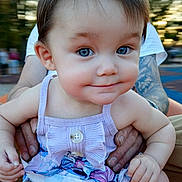 Hileigh is registered to the contest to win money with this photo: adult_hand, baby, blue_eyes, blurred_background, child, close_up, cute, family, floral_pattern, happy, infant, outdoor, person, portrait, purple_clothing, sitting, skin, smiling, summer, tattoo