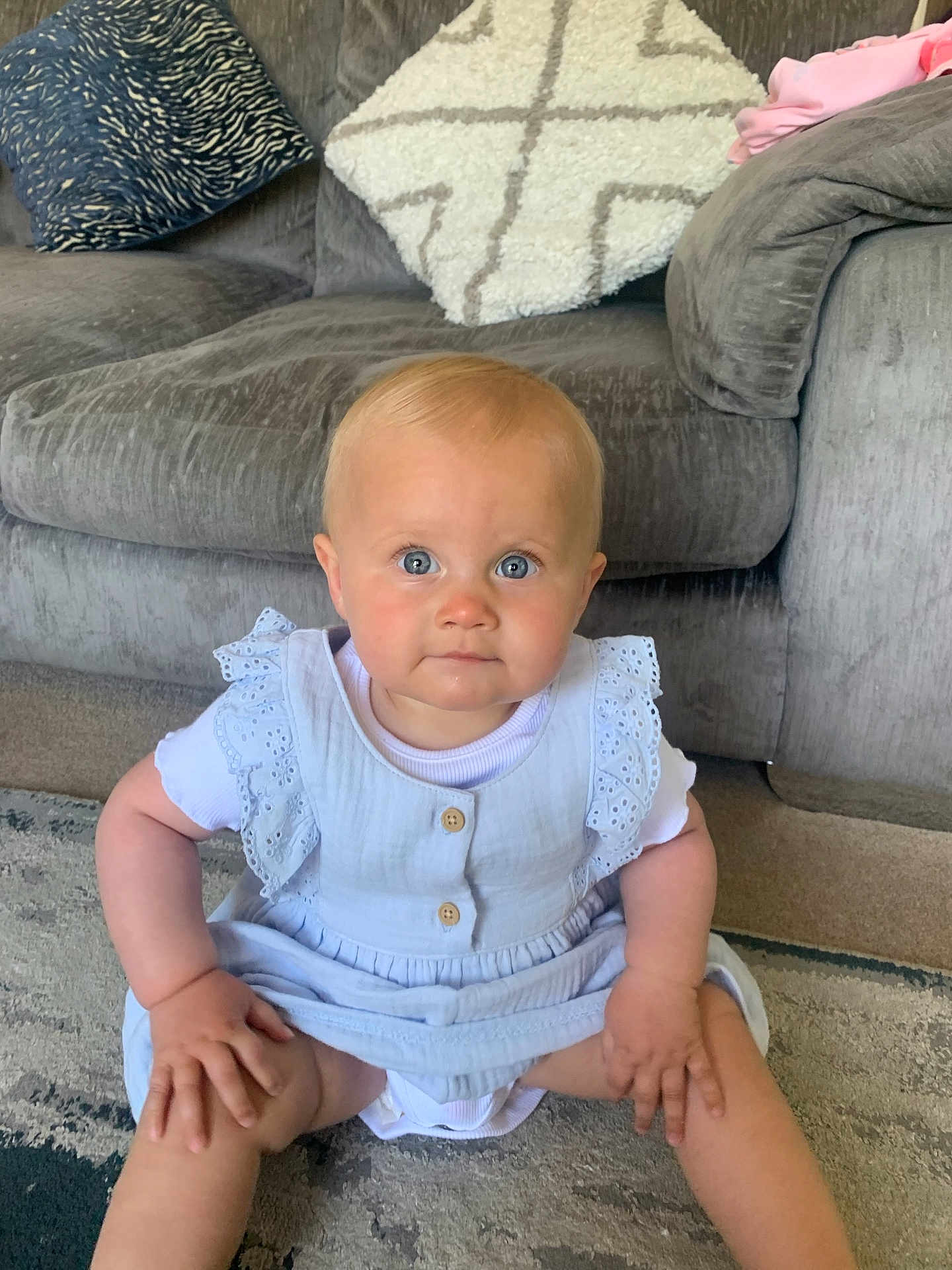 Ember is registered to the contest to win money with this photo: baby, child, infant, sitting, blue_eyes, dress, lace, hands, carpet, couch, pillows, indoor, furniture, cute, young_child, person, portrait, home, floor, serious_expression
