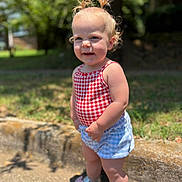 Charlotte is registered to the contest to win money with this photo: butterfly, casual_clothing, child, daylight, grass, greenery, hair_tied, happy, outdoor, portrait, sandals, shorts, sidewalk, smiling, standing, summer, sunlight, toddler, top, young_child