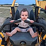Cy joined the competition — help win amazing prizes! baby, barefoot, child, construction_equipment, controls, daytime, equipment, field, grip, outdoor, person, rural, seat, shirt, shorts, sky, small_child, toddler, truck, yellow_vehicle