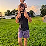 barefoot, beard, casual_clothing, child, clouds, daylight, grass, greenery, man, nature, outdoor, person, portrait, shorts, shoulder_ride, sky, sunset, toddler, trees, tshirt