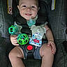 baby, infant, child, smiling, happy, car_seat, pacifier, toy, rattle, bib, elephant, diaper, seated, portrait, indoor, close_up, face, hands, baby_clothing, safety_harness