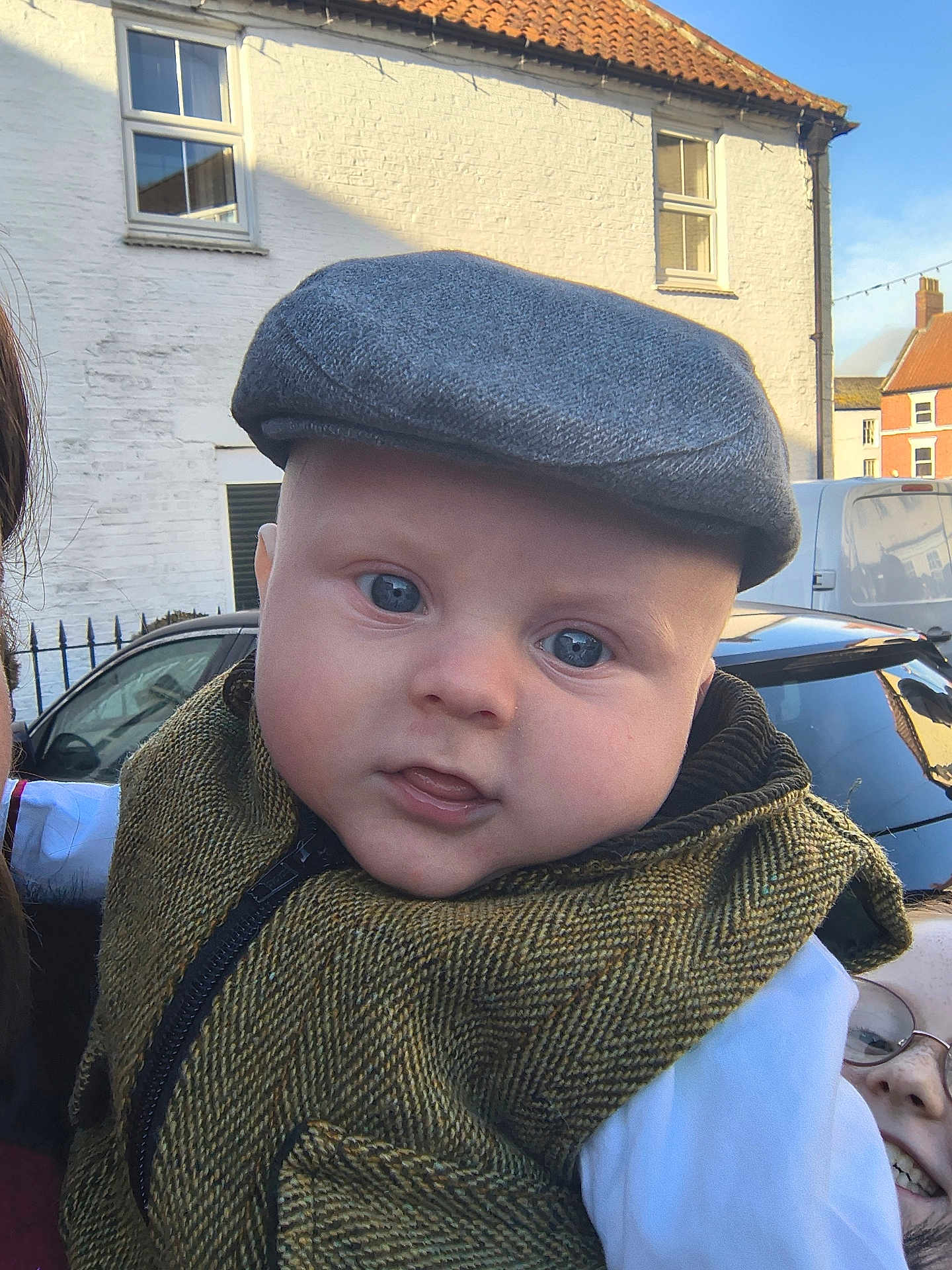 Lukas is registered to the contest to win money with this photo: baby, child, face, hat, cap, vest, clothing, outdoor, daylight, building, window, car, person, smile, glasses, headwear, fashion, portrait, curious, street