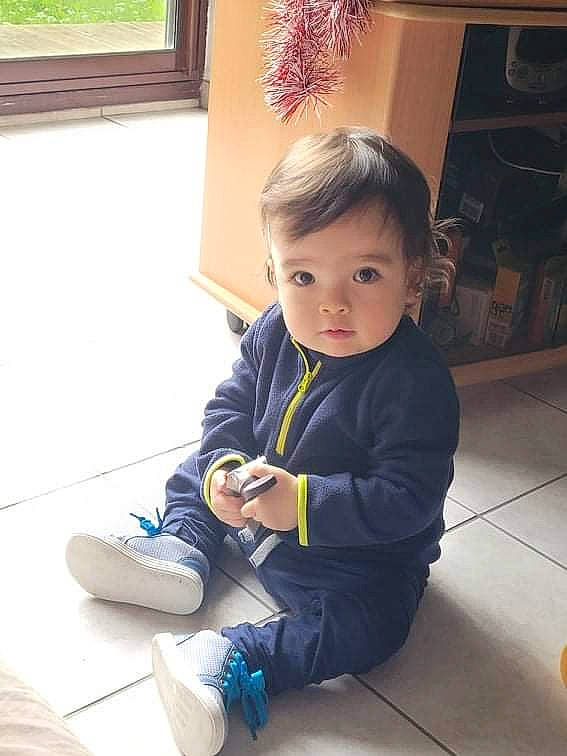 Ely a rejoint le concours — aidez-le/la à gagner de superbes lots ! baby, baby_toddler_clothing, child, face, floor, flooring, fun, hairstyle, happy, hardwood, head, leg, leisure, person, plant, sitting, skin, sleeve, sock, toddler