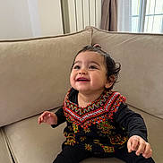 Lyna participe au concours pour gagner de l'argent avec cette photo : baby, child, smiling, sitting, couch, indoor, colorful_clothing, traditional_outfit, happy, face, window, curtains, furniture, sock, long_sleeve, patterned, young_child, portrait, cute, cozy