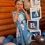 Ariana is registered to the contest to win money with this photo: baby_shower, balloons, big_sister_sash, blocks, blue_dress, celebration, child, decorations, festive, flower_crown, girl, hand_gesture, happy, heart_shape, indoor, letters, party, pink_crocs, smiling, wooden_wall