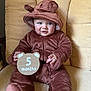 baby, child, infant, onesie, hood, ears, bear_costume, sign, wooden_sign, months, cushion, chair, furniture, cute, smiling, sitting, indoors, portrait, soft_texture, clothing