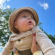 Nathan is registered to the contest to win money with this photo: baby, child, infant, hat, beige_clothing, outdoor, blue_sky, clouds, hands, nail_polish, red_nails, cute, portrait, looking_up, nature, greenery, person, soft_fabric, daylight, expression