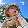 baby, child, infant, hat, beige_clothing, outdoor, blue_sky, clouds, hands, nail_polish, red_nails, cute, portrait, looking_up, nature, greenery, person, soft_fabric, daylight, expression