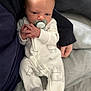 baby, infant, pacifier, onesie, sheep_pattern, hand, face, clothing, adult_hand, sitting, cozy, soft_lighting, bed, blanket, person, newborn, cute, portrait, indoor, resting